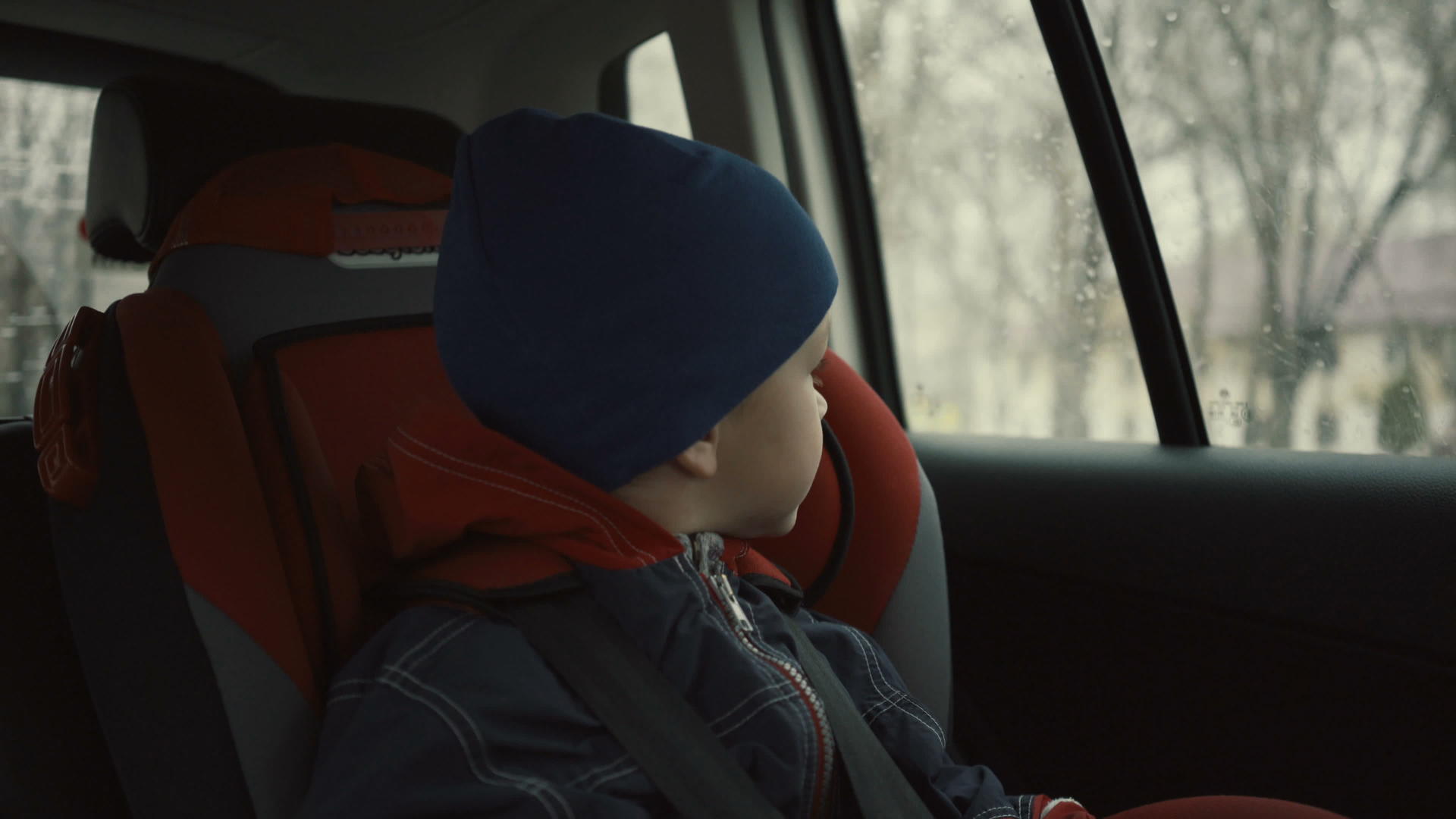 男孩坐在儿童座位的车里在雨季看着窗外视频的预览图