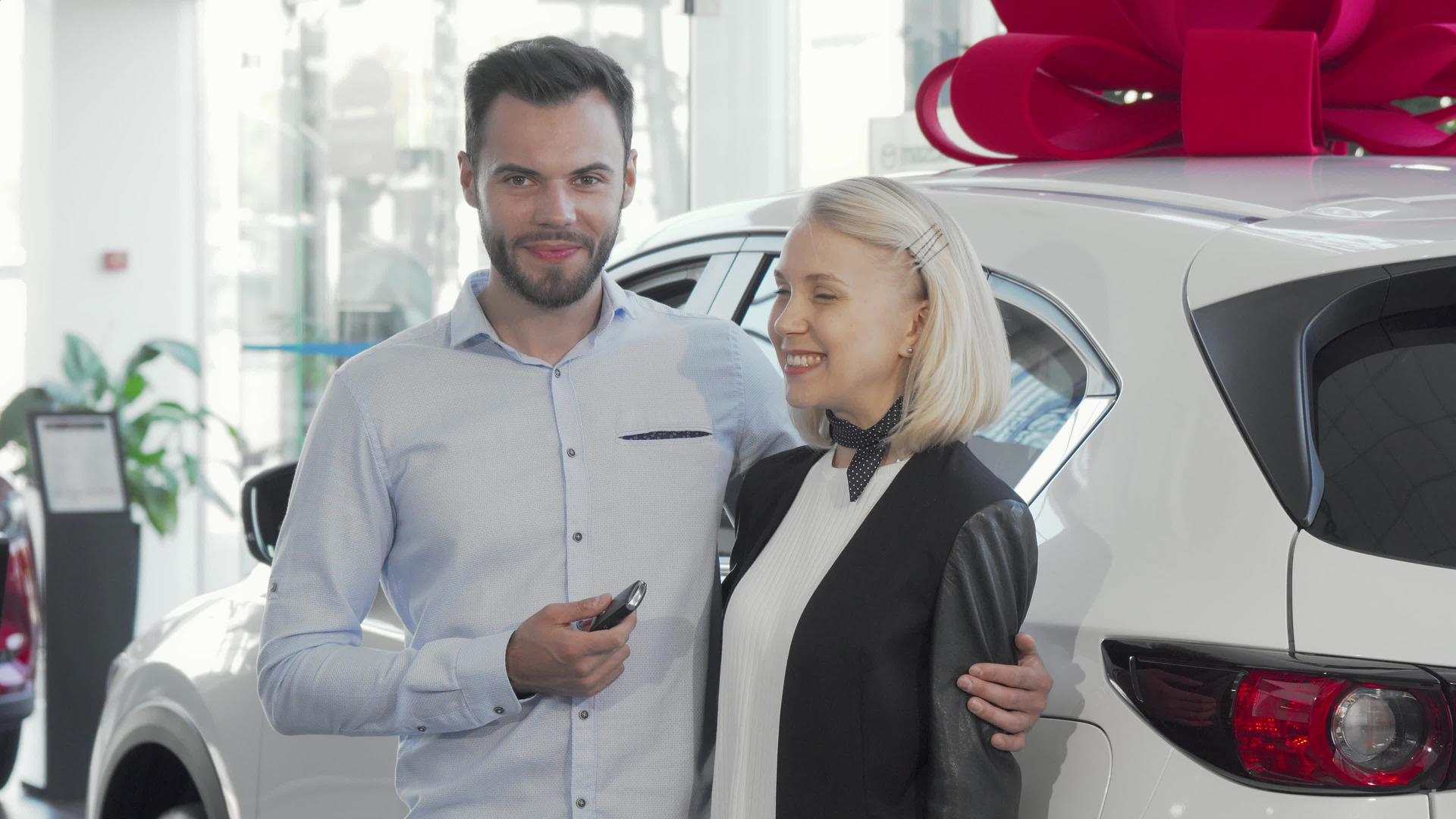 一对幸福的年轻夫妇站在他们的新车旁边在经销店视频的预览图