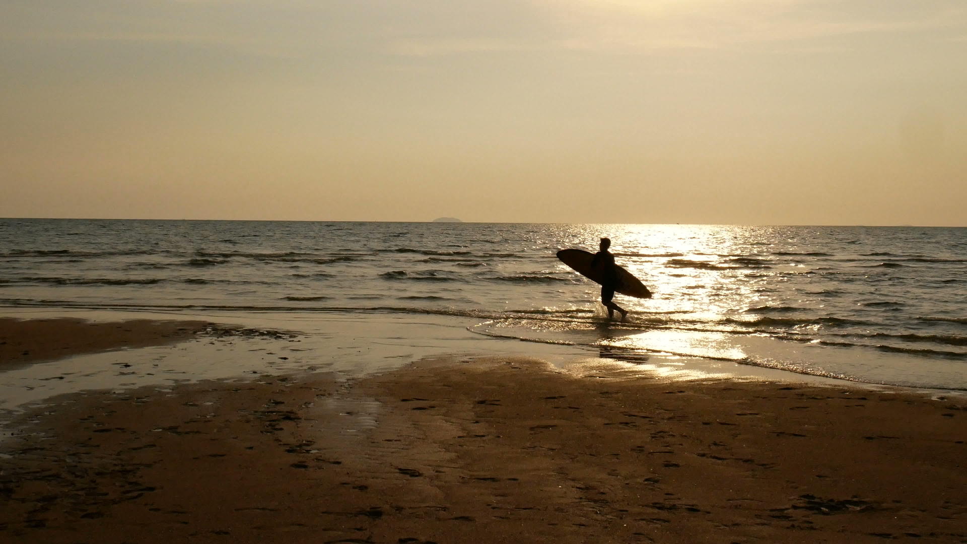 热带海滩日落时冲浪者带着长长的冲浪板踏入海中视频的预览图