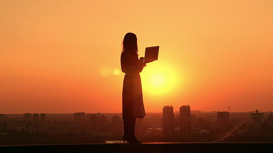 日出时妇女使用笔记本电脑、户外城市风景视频的预览图