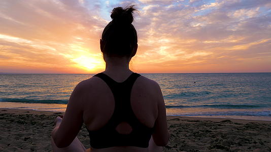 坐在沙滩上练习瑜伽的女人的轮廓视频的预览图