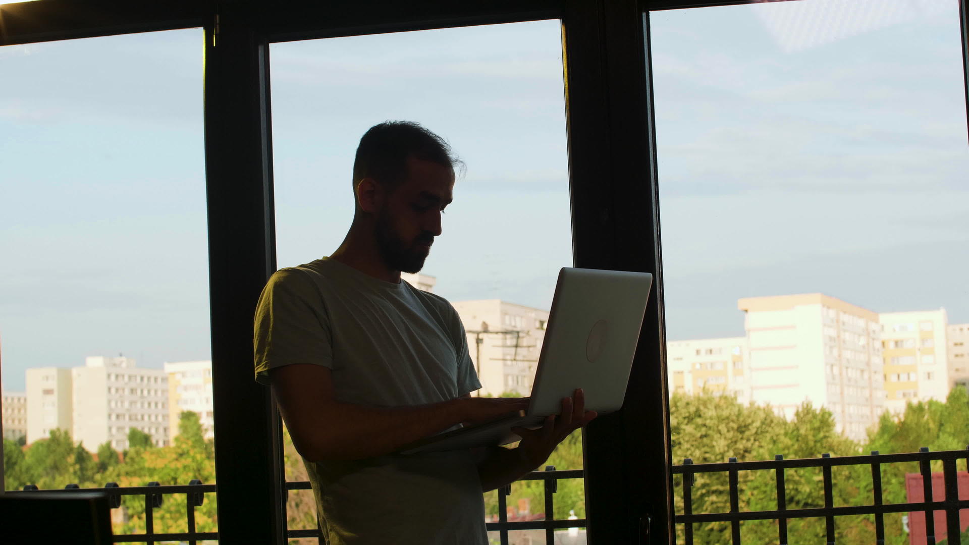 一个男人站在窗户旁边手里拿着笔记本电脑工作视频的预览图