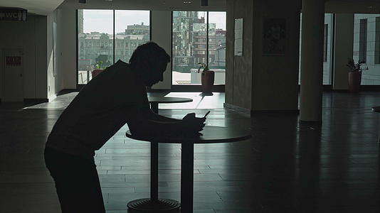 一个年轻人坐在房间前厅的桌子上拿着一个电话身影笑着视频的预览图