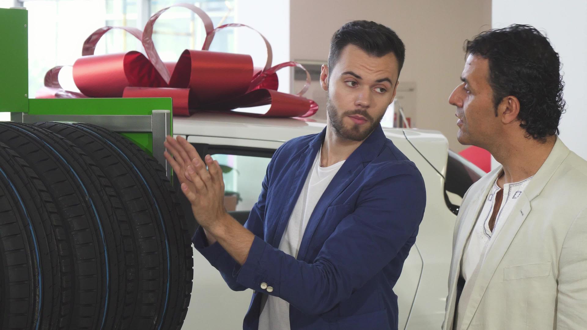 年轻的推销员帮助成熟的客户选择汽车轮胎视频的预览图