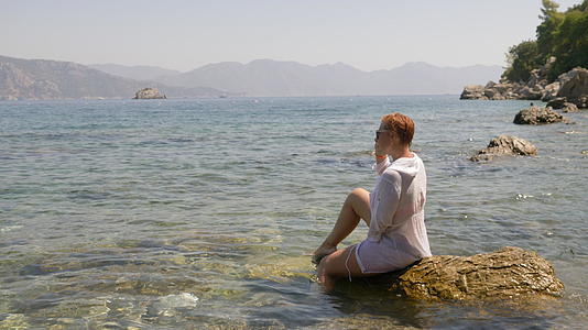夏天旅行时轻松的女人坐在波浪中的大石头上在山景上快乐视频的预览图