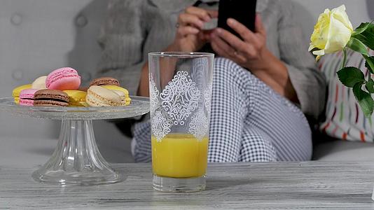 女性用智能手机在沙发上喝橙汁视频的预览图