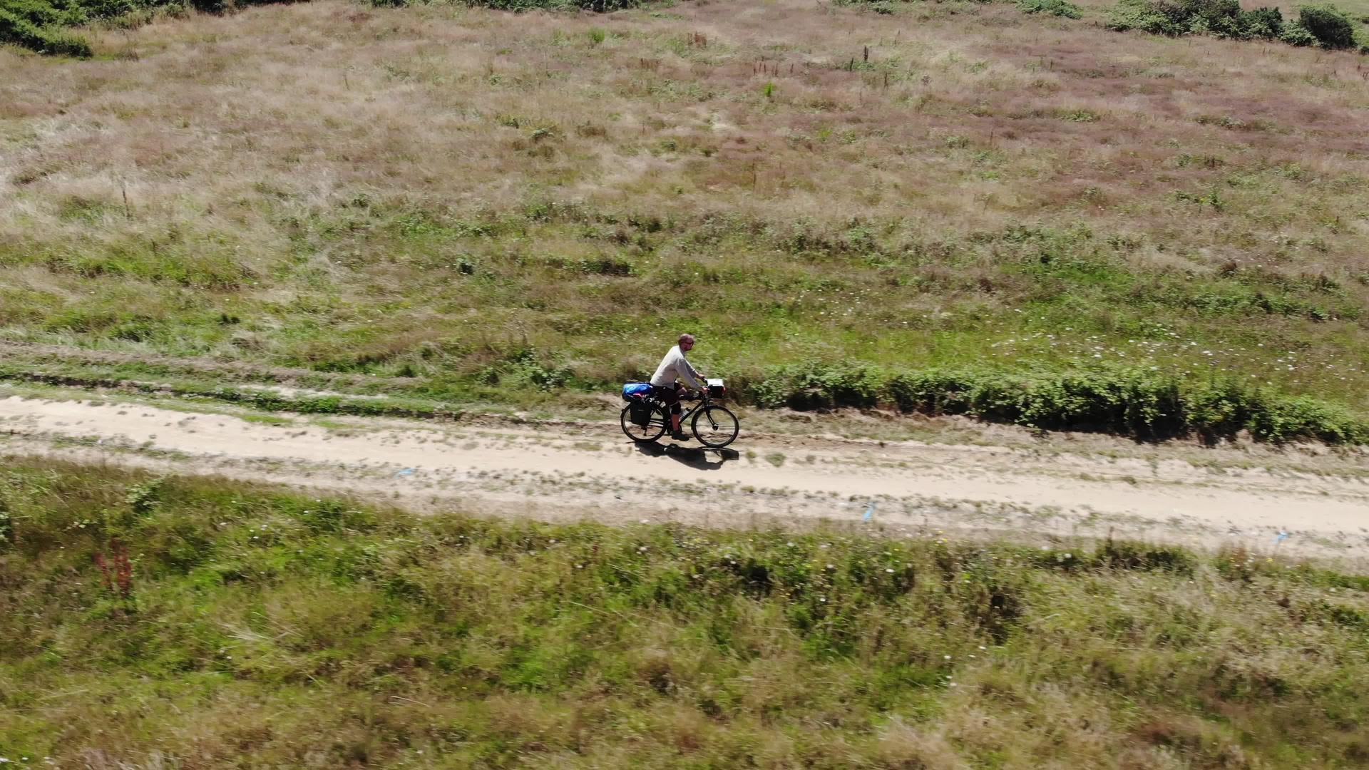 在田野和森林之间专业骑自行车的人沿着美丽的乡村道路行驶视频的预览图