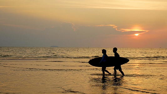 年轻快乐的冲浪男女日落时在热带海滩上使用长冲浪板视频的预览图
