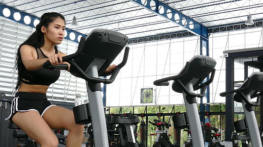 年轻女性在健身中心锻炼女运动员在健身房骑固定自行车视频的预览图