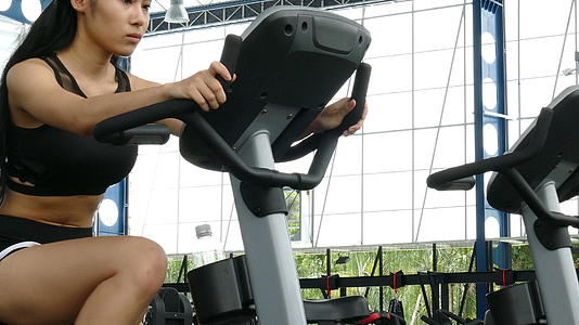 年轻女性在健身中心锻炼女运动员在健身房骑固定自行车视频的预览图