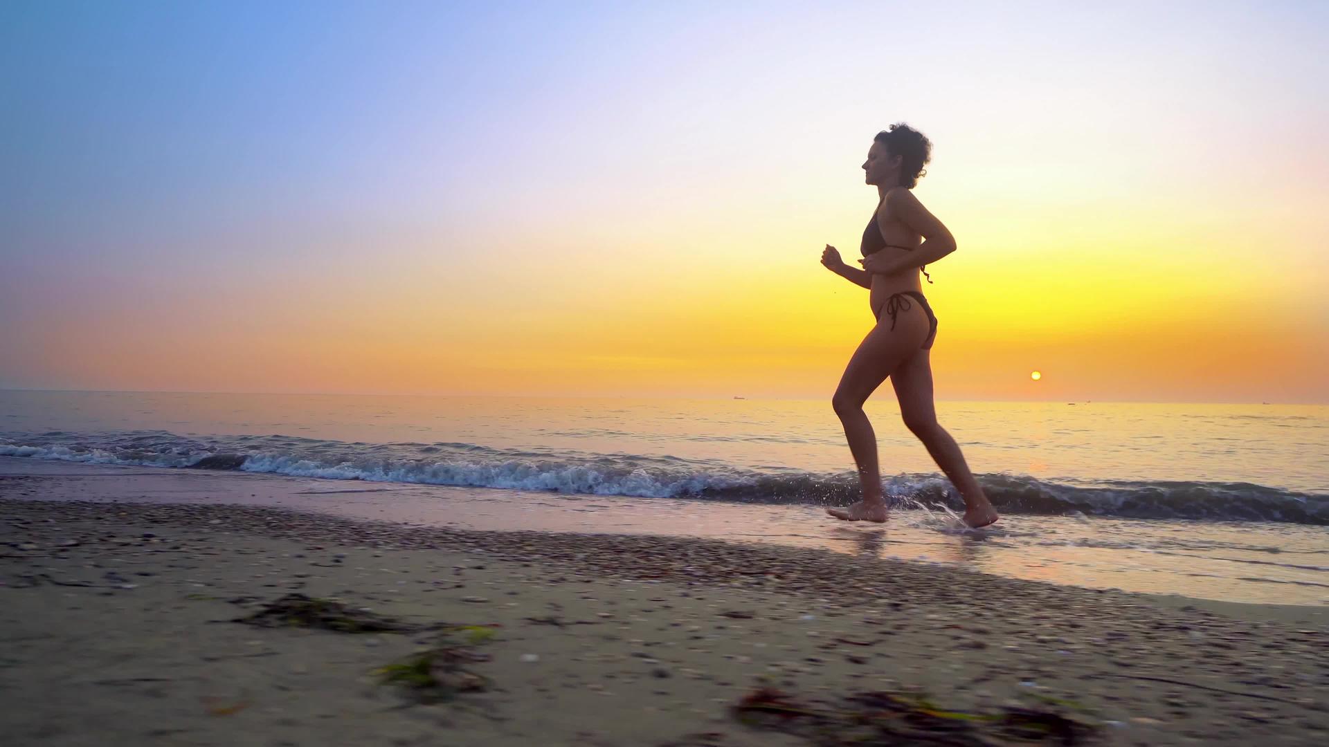 赤脚运动女性比基尼在日落时在空海滩上跑步视频的预览图