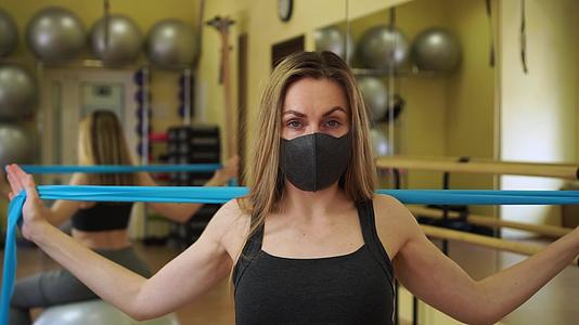 年轻女运动员戴着黑色防护口罩在空荡荡的健身房里伸展视频的预览图