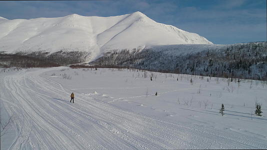 在一个阳光明媚的冬天 男子在山上徒步旅行 用登山杖鸟瞰无人机视频的预览图