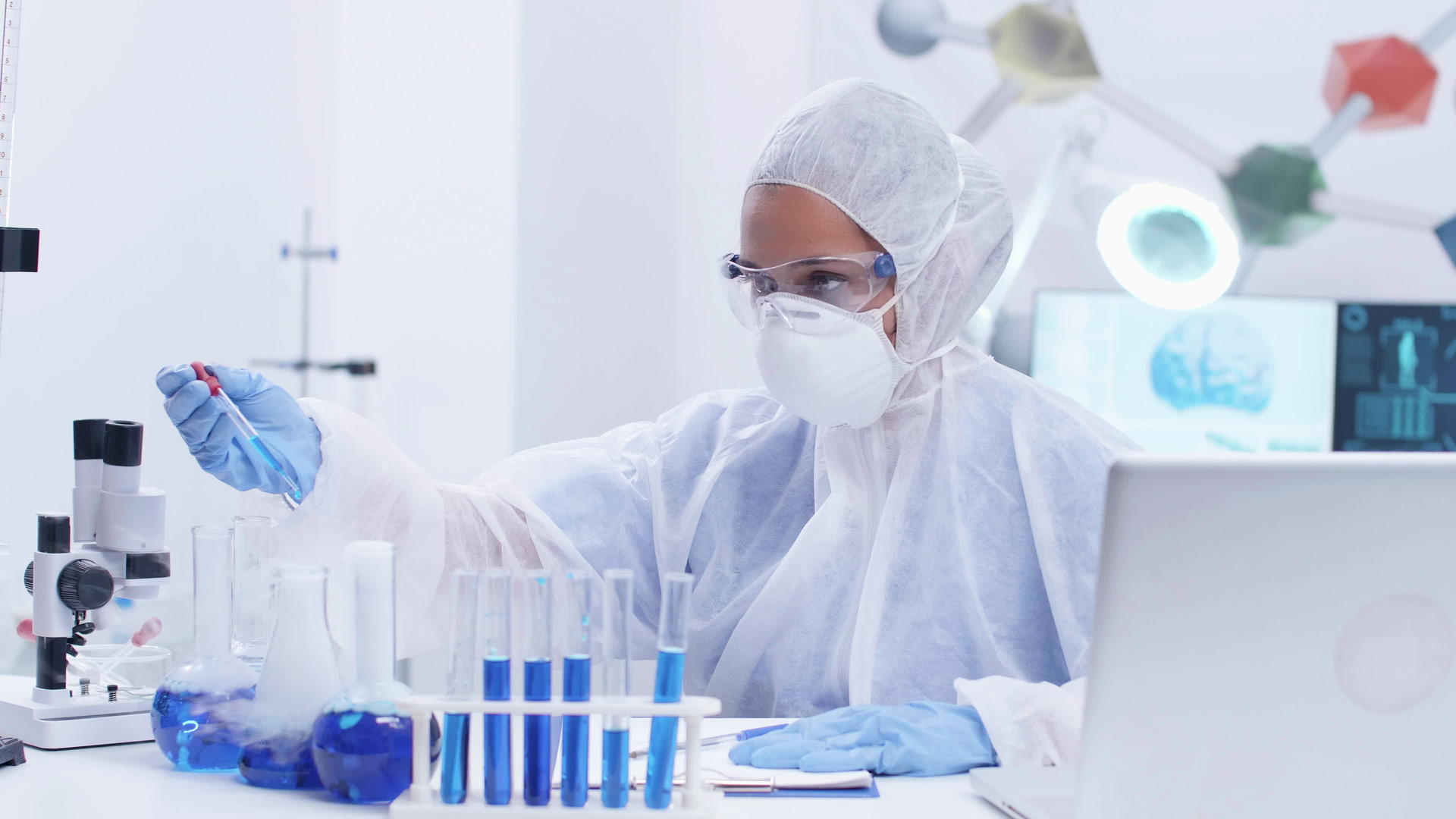 专注于工作服防护设备的女性科学家使用蓝色液体进行科学研究视频的预览图