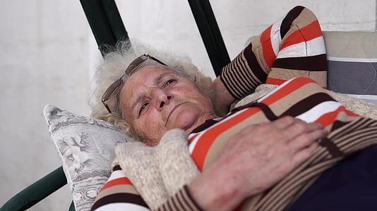 老妇人躺在门廊的摇摆床上看着悲伤的距离视频的预览图