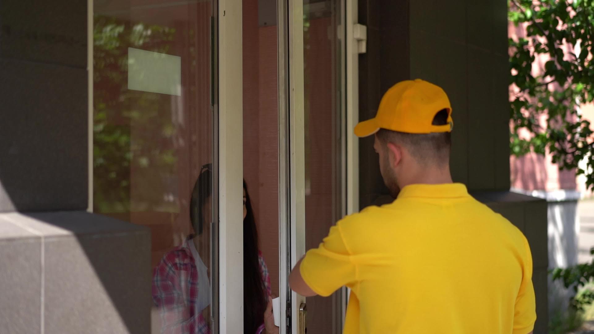 穿着黄色制服的快递员把披萨盒给了门口的女人视频的预览图