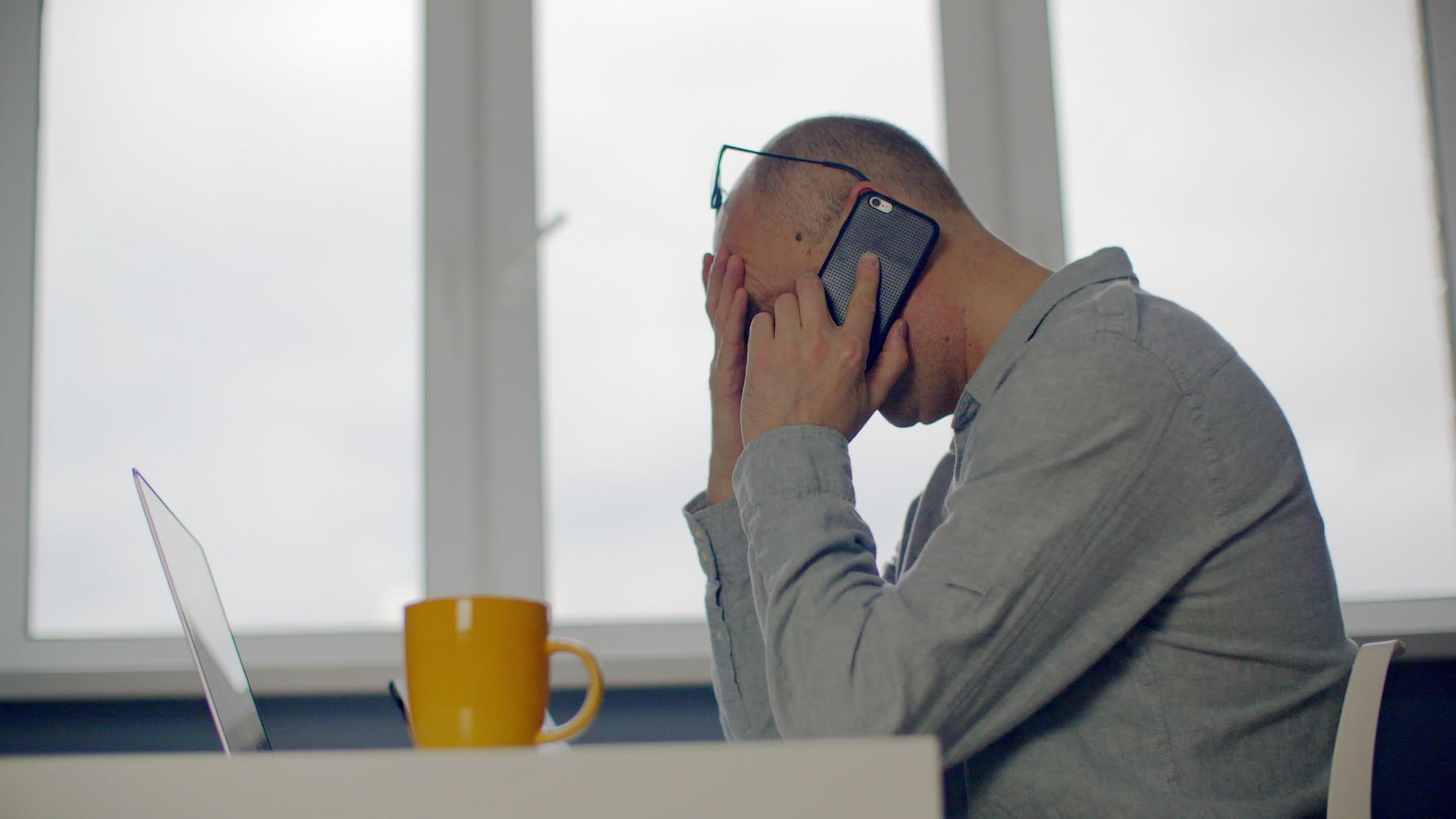 沮丧的成年商人在办公室手机前用笔记本电脑说话心烦意乱视频的预览图