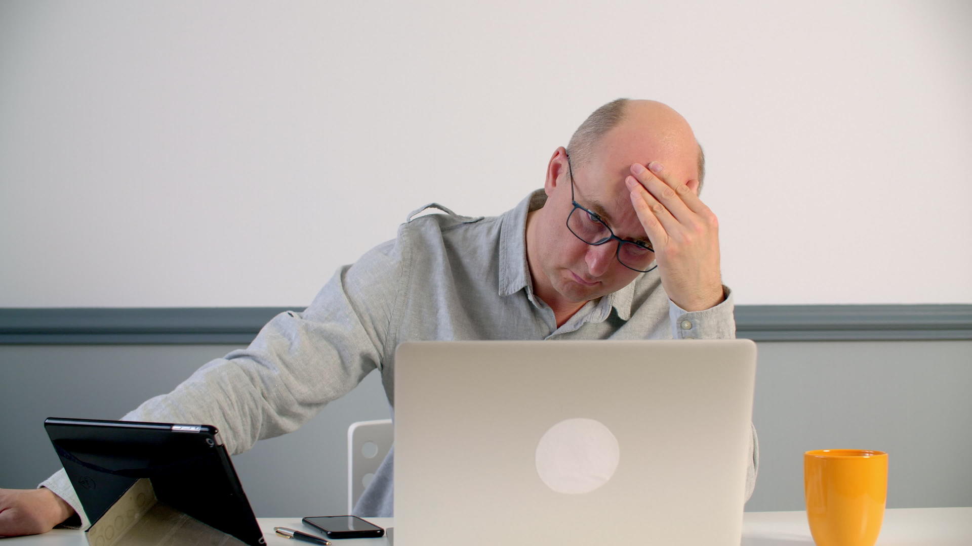 当一个抑郁的男人在办公室用笔记本电脑努力工作时他会触摸他的额头视频的预览图