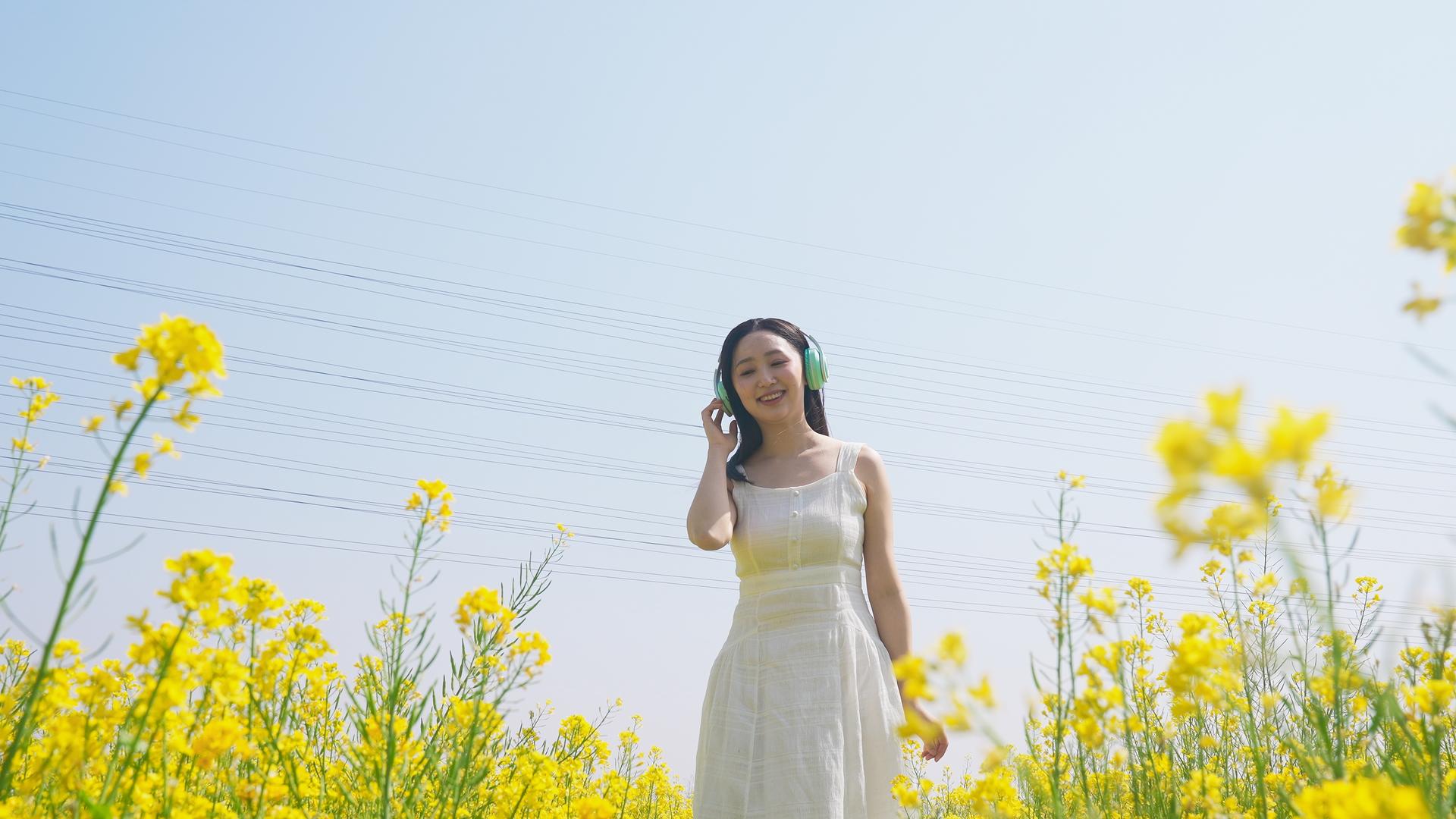 长裙女子在油菜田里带着耳机听音乐视频的预览图