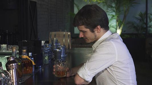 年轻帅哥一个人在酒吧喝威士忌对着镜头开心地笑着视频的预览图