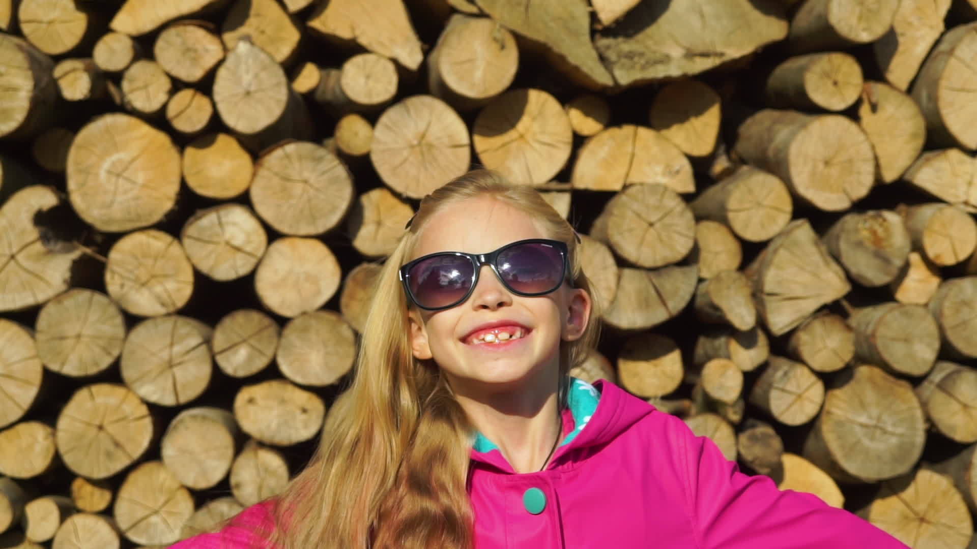 女孩和女孩穿着粉色外套和太阳镜背景中堆满了木头视频的预览图