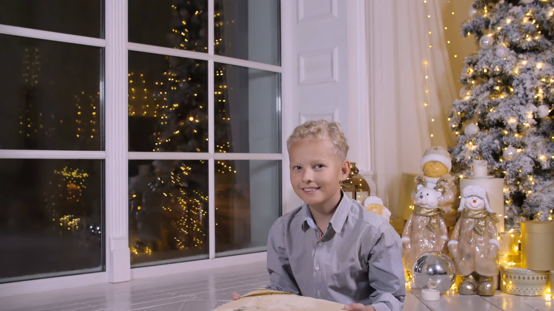 金发男孩把圣诞礼物盒扔在圣诞树底部的圣诞树上视频的预览图