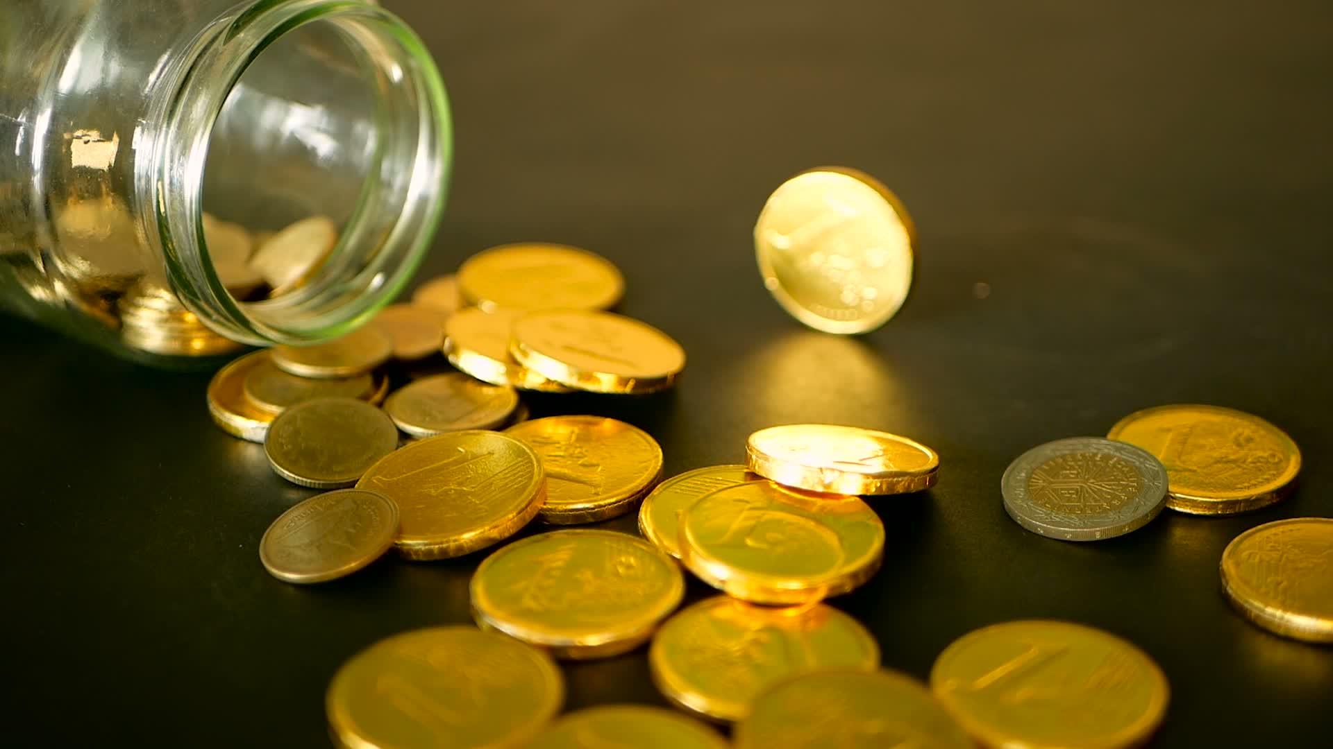 黑色桌子上的金币和旋转便士黄色硬币从罐子里掉了下来视频的预览图