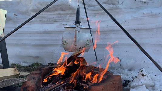 旅游茶壶挂在冬天自然燃烧的营火上视频的预览图