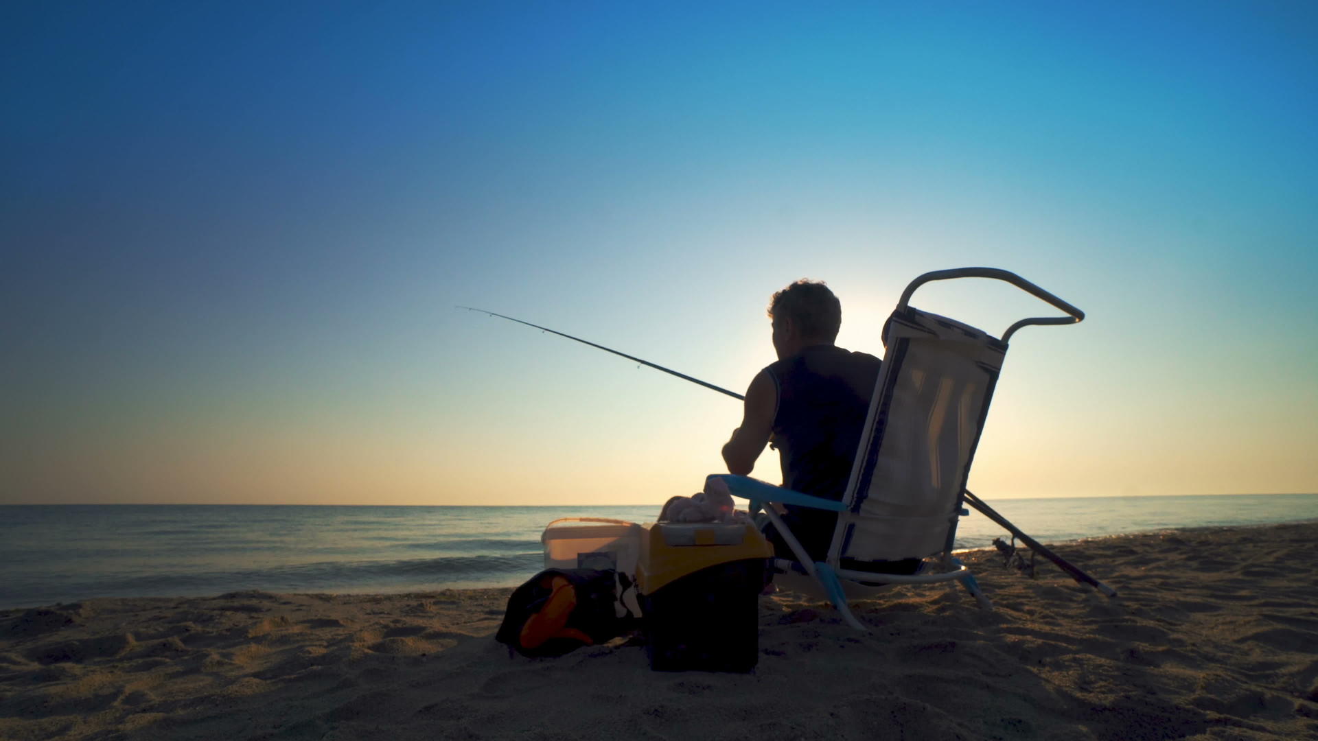 年轻人在湖边钓鱼日落时坐在海滩上视频的预览图