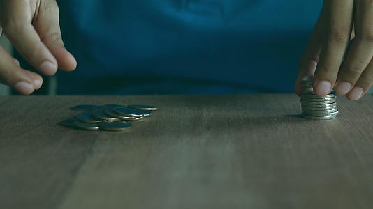穿着蓝色衬衫的女人在棕色木桌上堆积硬币视频的预览图