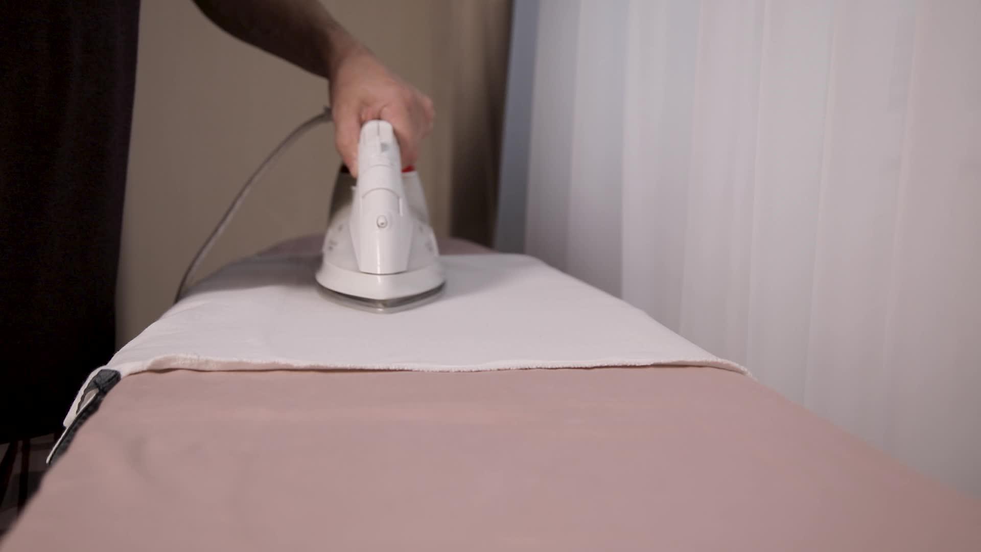 一个男人用白电铁在熨衣板上熨床单视频的预览图
