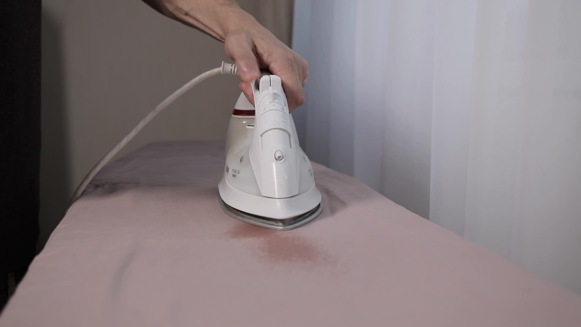 一个男人用白电铁在熨衣板上熨床单视频的预览图