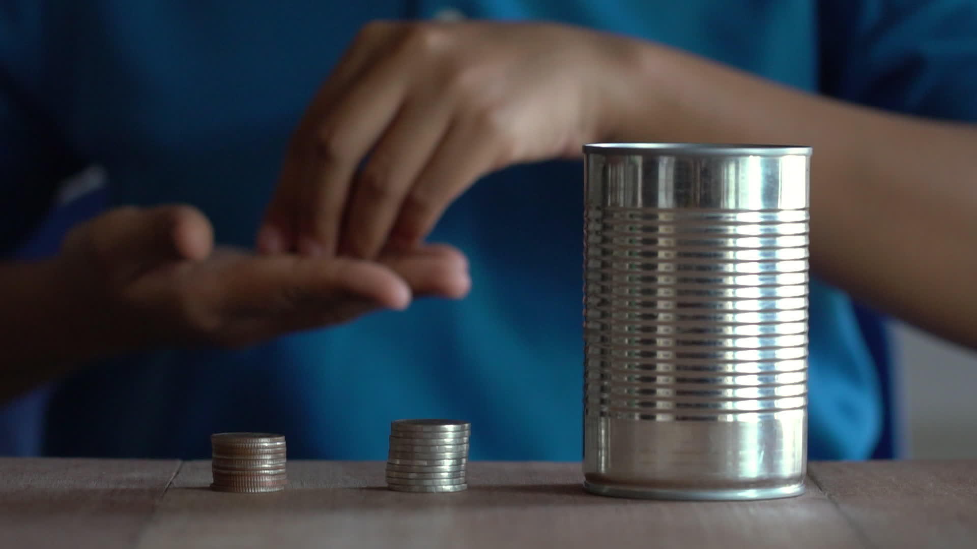一个穿着蓝色衬衫的女人把一枚硬币扔进一个老罐子里放在一张棕色的木桌上视频的预览图
