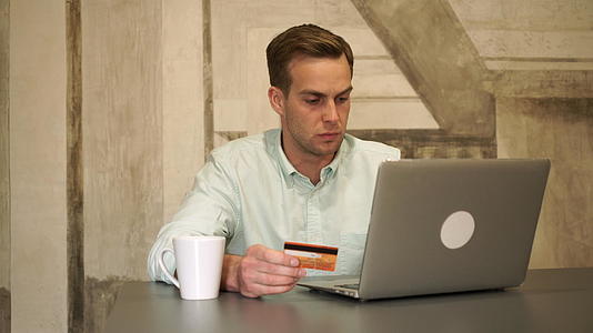 英俊的年轻人用电脑和信用卡购物视频的预览图