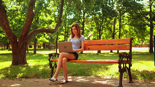 年轻女性在坐在长凳上的电脑上打字视频的预览图