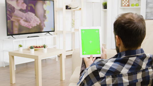 男人在电视上看电影还有一台绿屏数字平板电脑视频的预览图