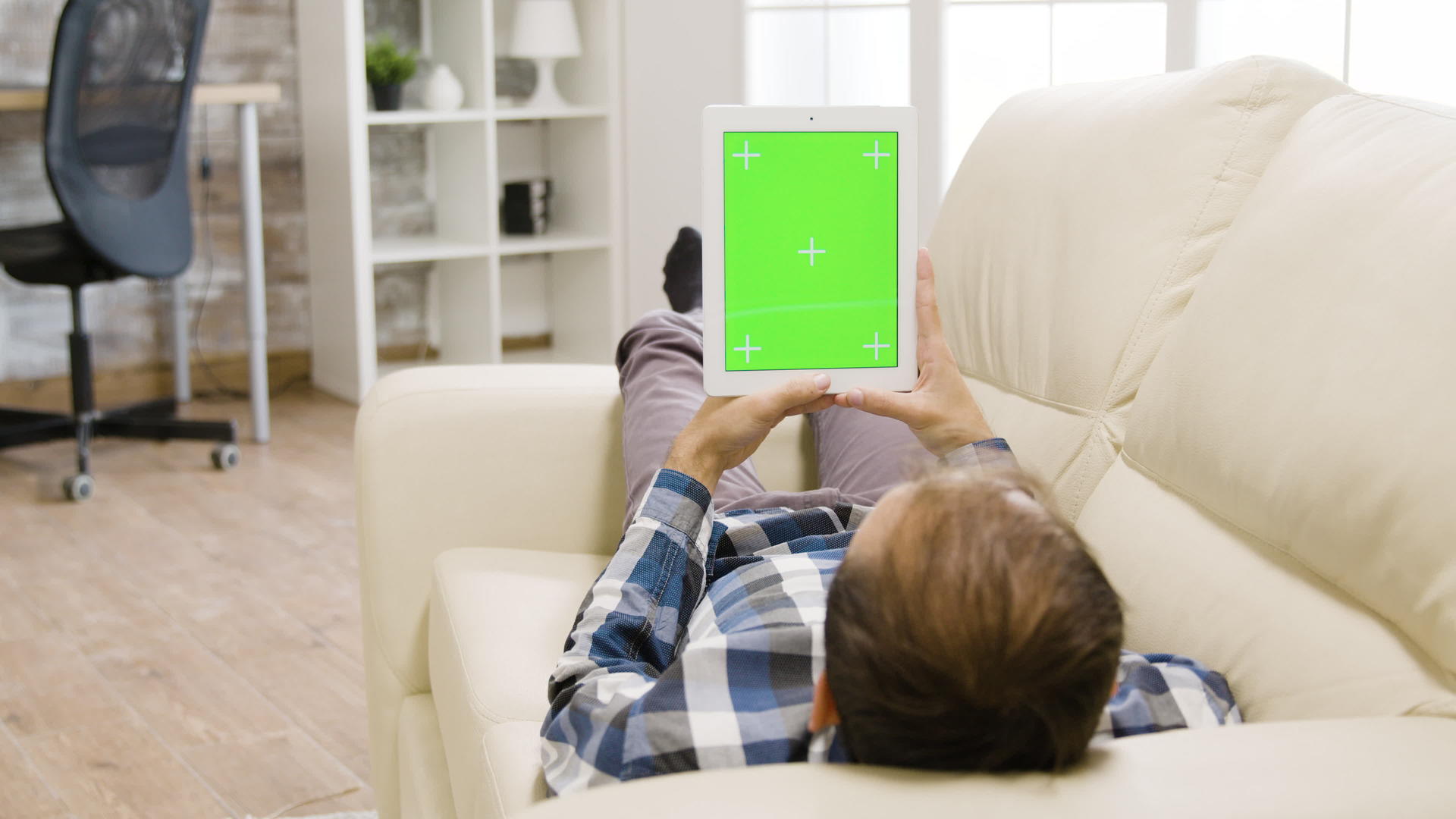 坐在明亮的客厅里的年轻人拿着一台绿色的数字平板电脑视频的预览图