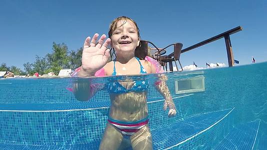 这个可爱的小女孩有一条胳膊和一个飞溅的相机在温暖的温泉池里半水下视频的预览图