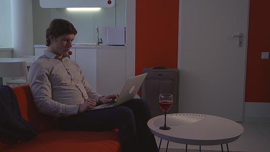 男人在公寓里用笔记本电脑喝酒视频的预览图