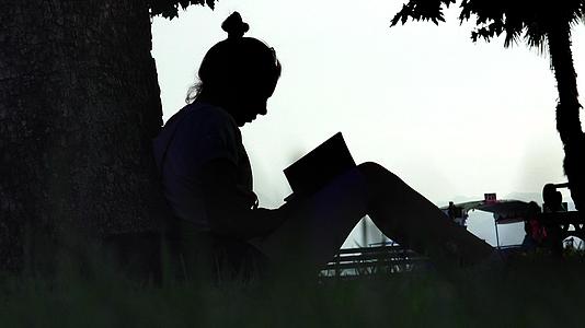在公园树旁读书的年轻迷人的年轻女子双影女郎视频的预览图
