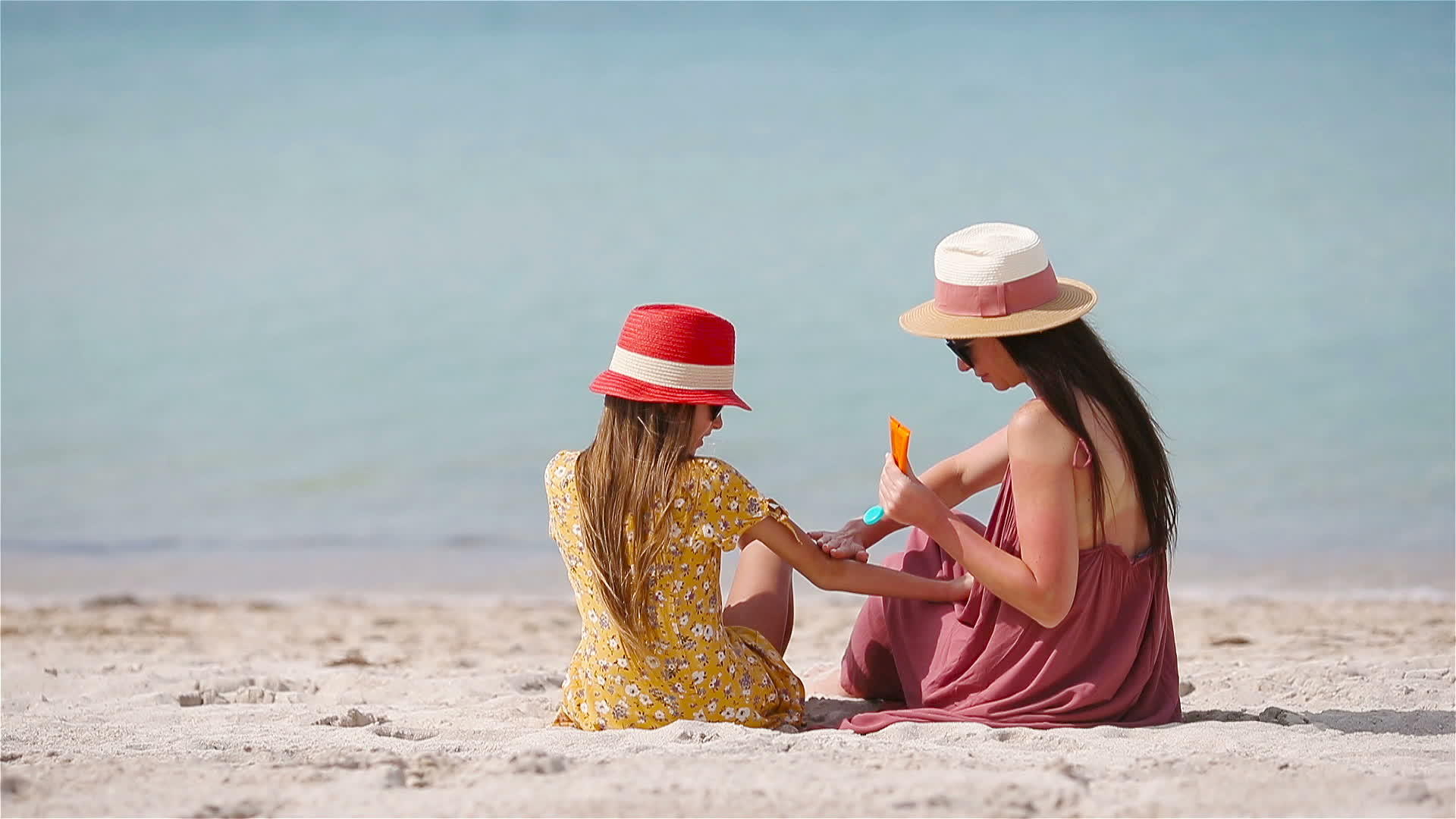 年轻的母亲在海滩上给女儿的鼻子涂上防晒霜以保护她的阳光视频的预览图