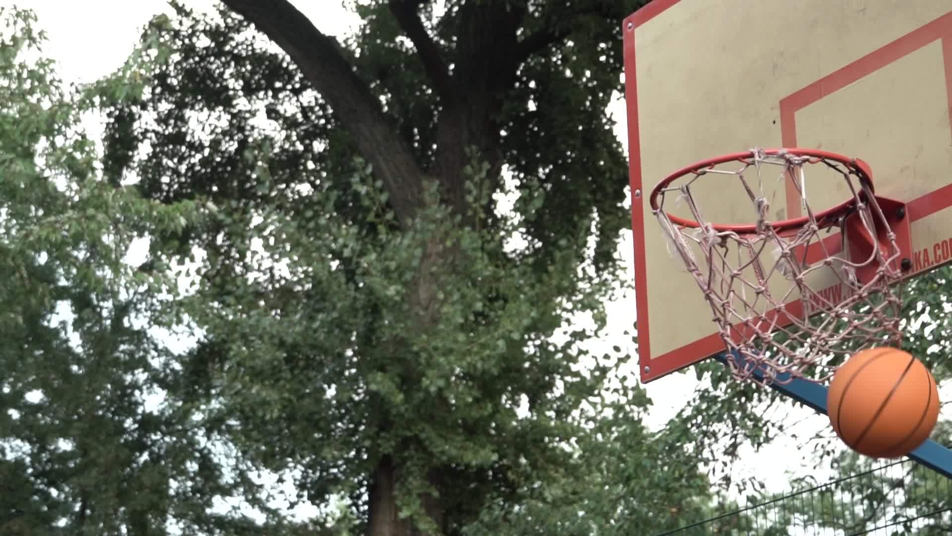 在树荫下的室外法庭上抛出橙色篮球击中篮筐达到目标视频的预览图