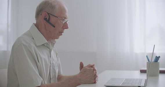 老人通过视频电话与朋友或同事交流观看笔记本电脑视频的预览图