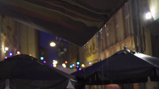 灯笼和彩色灯光挂着大雨落在欧洲老城区狭窄街道的树冠上视频的预览图
