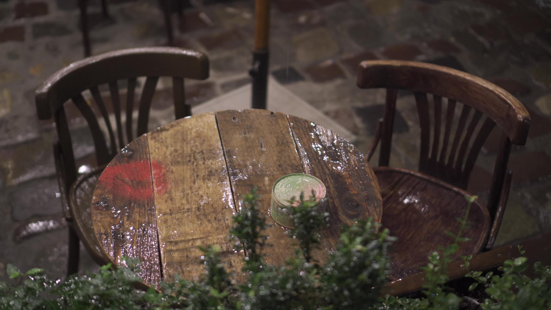 晚上在大雨中潮湿的桌子和湿木家具落在街上的咖啡馆里视频的预览图