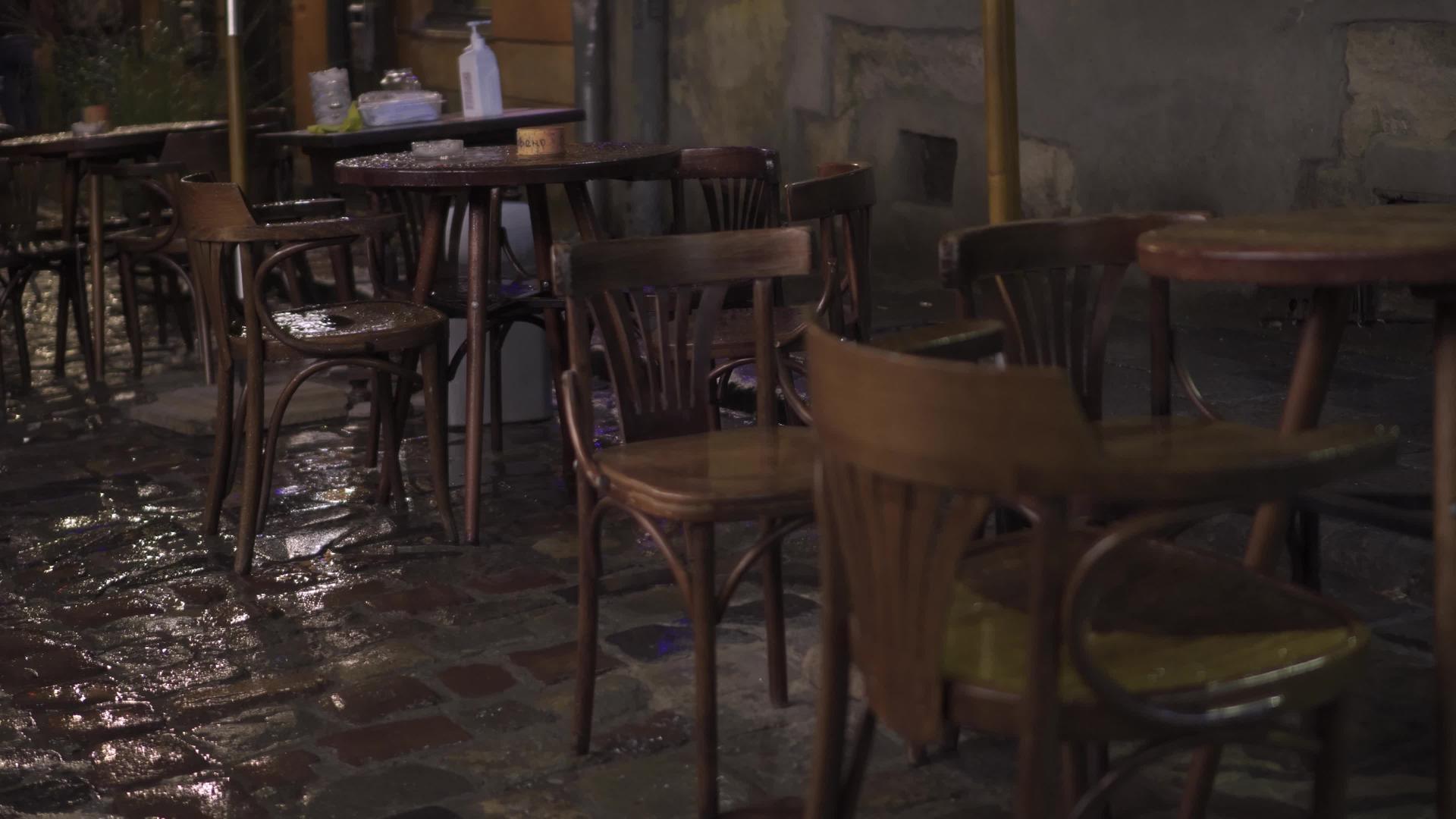 晚上潮湿的街头咖啡馆的湿木家具桌椅在倾盆大雨中落在潮湿的街道上视频的预览图