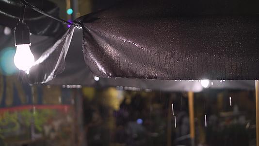 晚上在倾盆大雨中户外老城街的咖啡馆里挂着天篷灯和灯泡视频的预览图