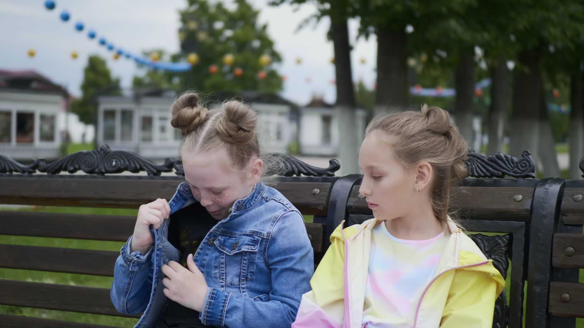 坐在长凳上的两个十几岁的女孩朋友看着夹克口袋里的一个视频的预览图