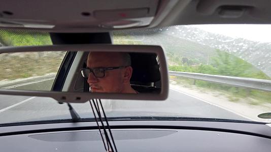 在雨中驾驶汽车的男性司机的肖像在后视镜中看到视频的预览图