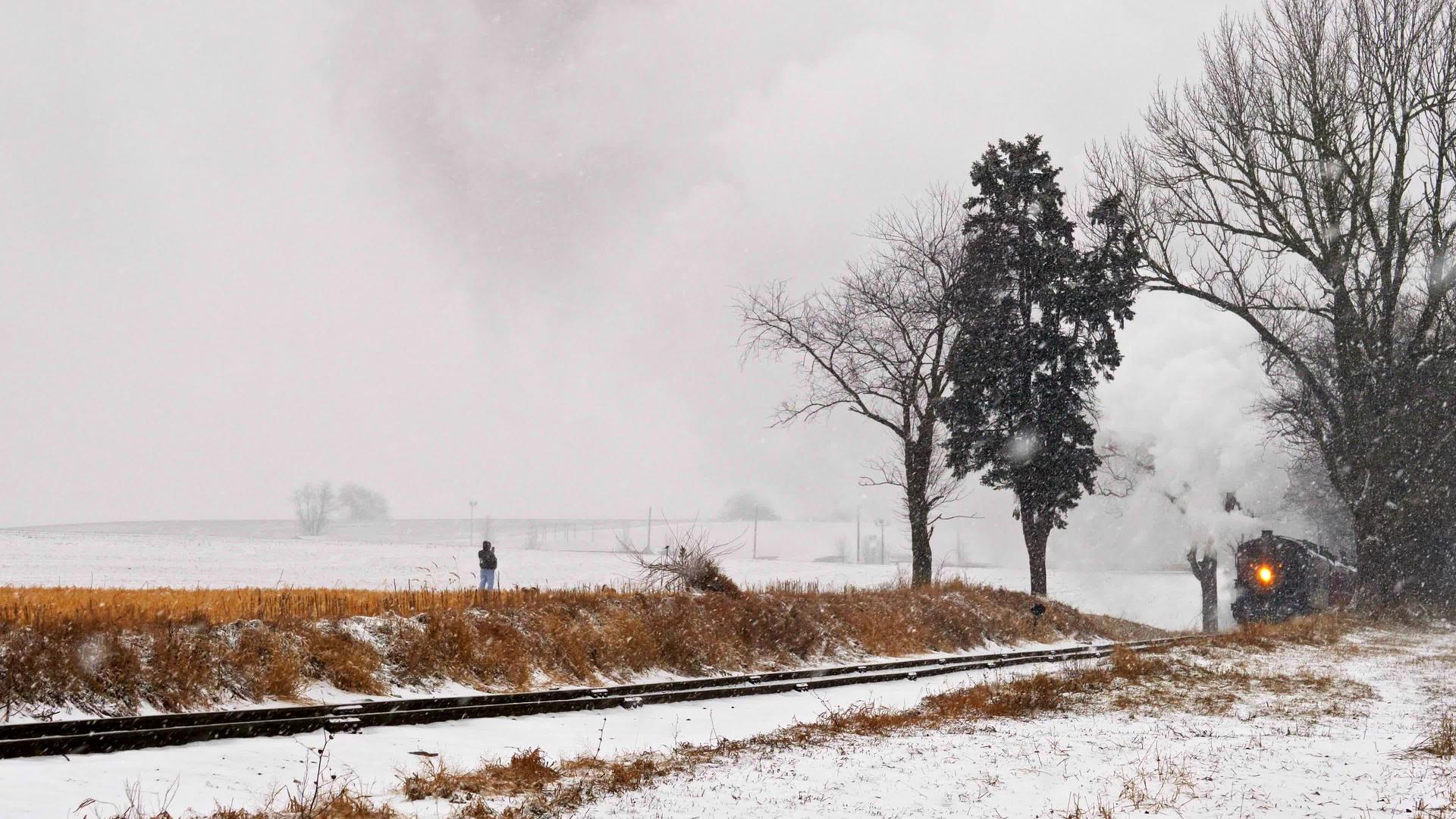 一名男子在一条铁轨公路上行走他的狗作为蒸汽机乘客车驶近暴风雪视频的预览图